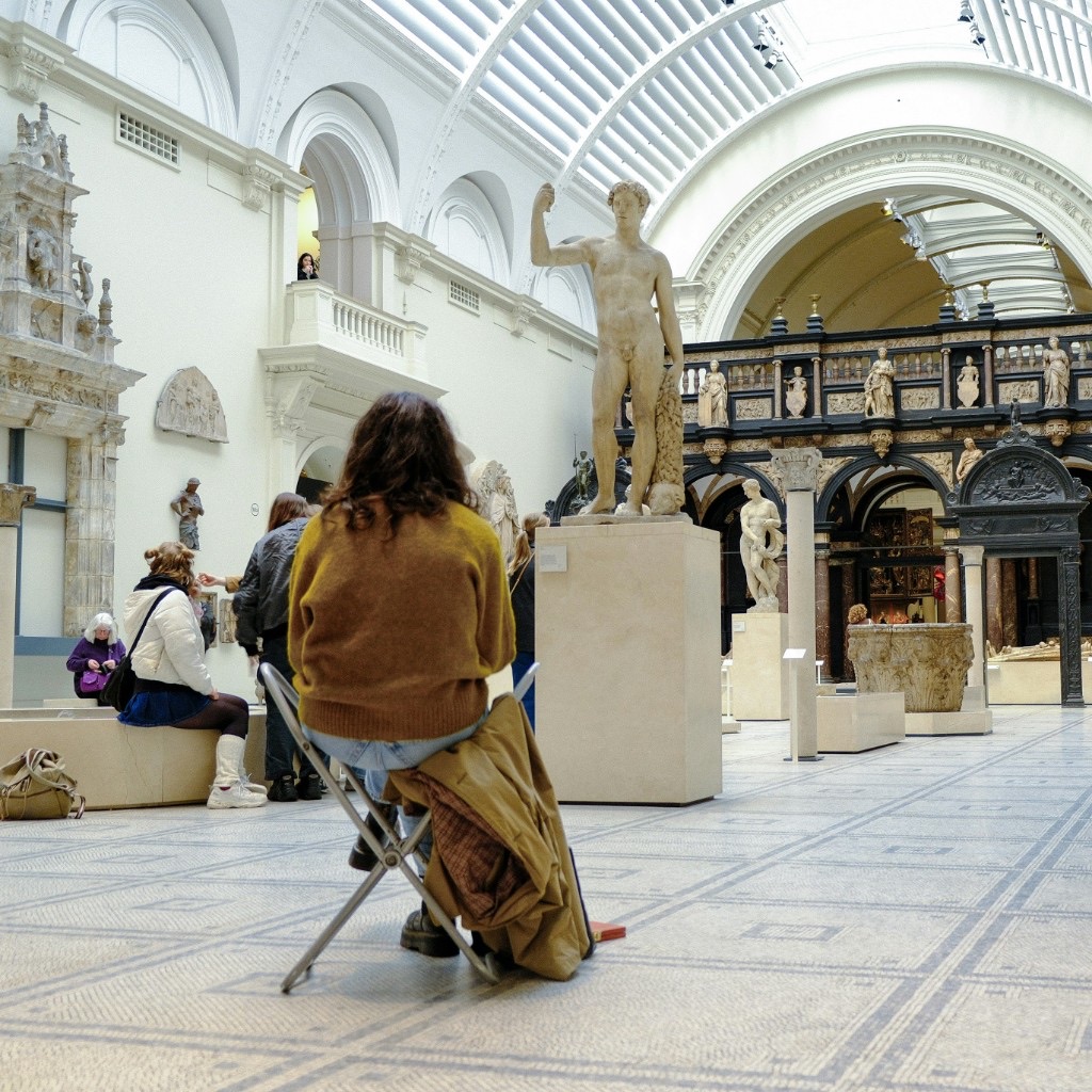 Visitor seated in a sunlit classical sculpture gallery