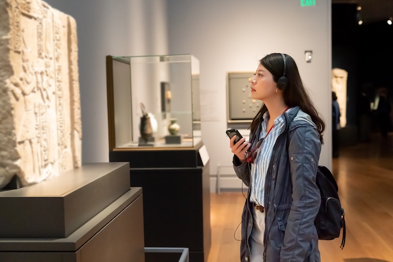 A visitor with headphones and a smartphone viewing artefacts in a museum gallery