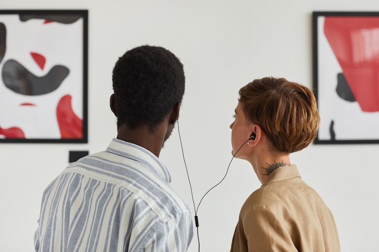 Two visitors sharing an audio guide while looking at paintings in a museum